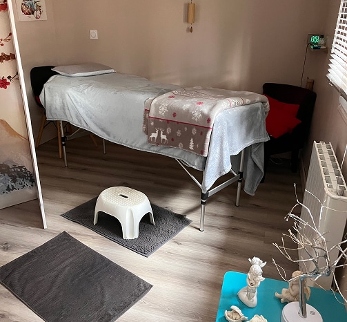 Table de massage avec couverture polaire à motifs de rennes et flocons, tabouret blanc, tapis gris, affichage horloge 13:03.
