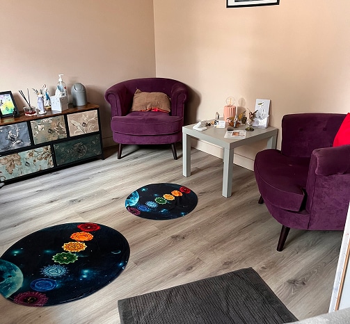 Coin salon détente avec deux fauteuils violets, une table basse grise et deux tapis ronds représentant les chakras sur un sol stratifié clair.